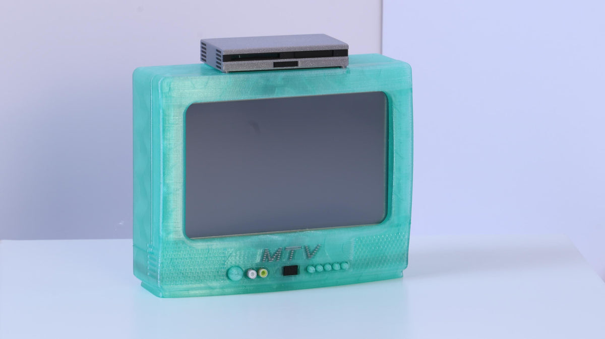 May include: A translucent mint green television set with a dark gray screen and the letters MTV embossed on the front panel. A small, rectangular, silver-colored electronic device is positioned on top of the television unit.